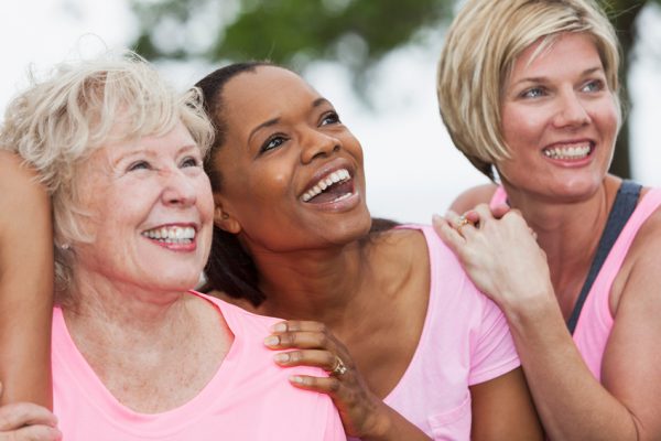 Three women in pink shirts lookup upward toward the sky.