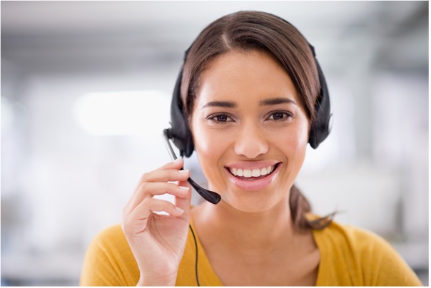 A smiling customer service rep in a yellow shirt holding her headphones