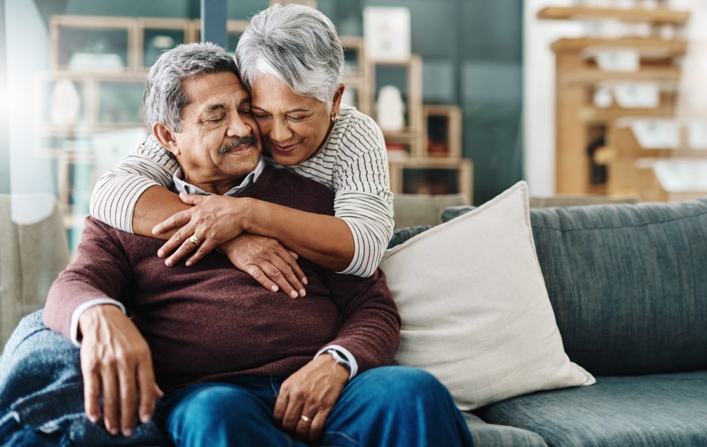 cheerful elderly woman hugging her husband who's in a wheelchair at home