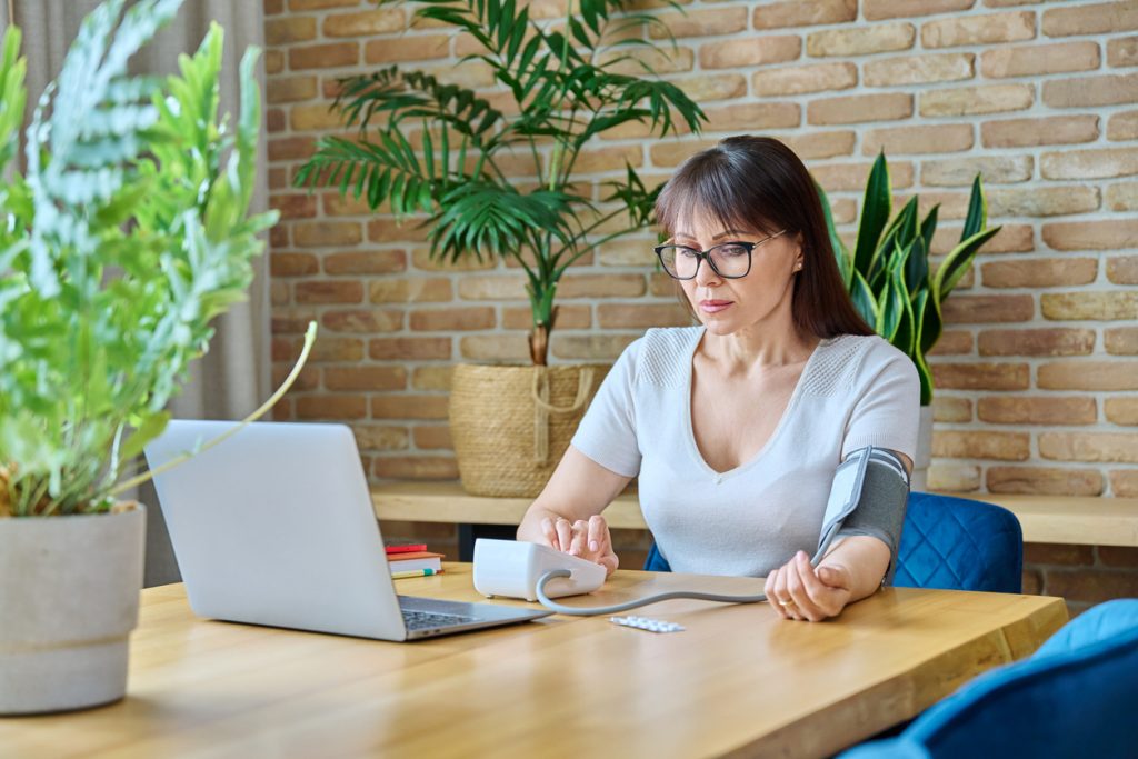 Middle-aged woman sitting at table at home, measuring blood pressure