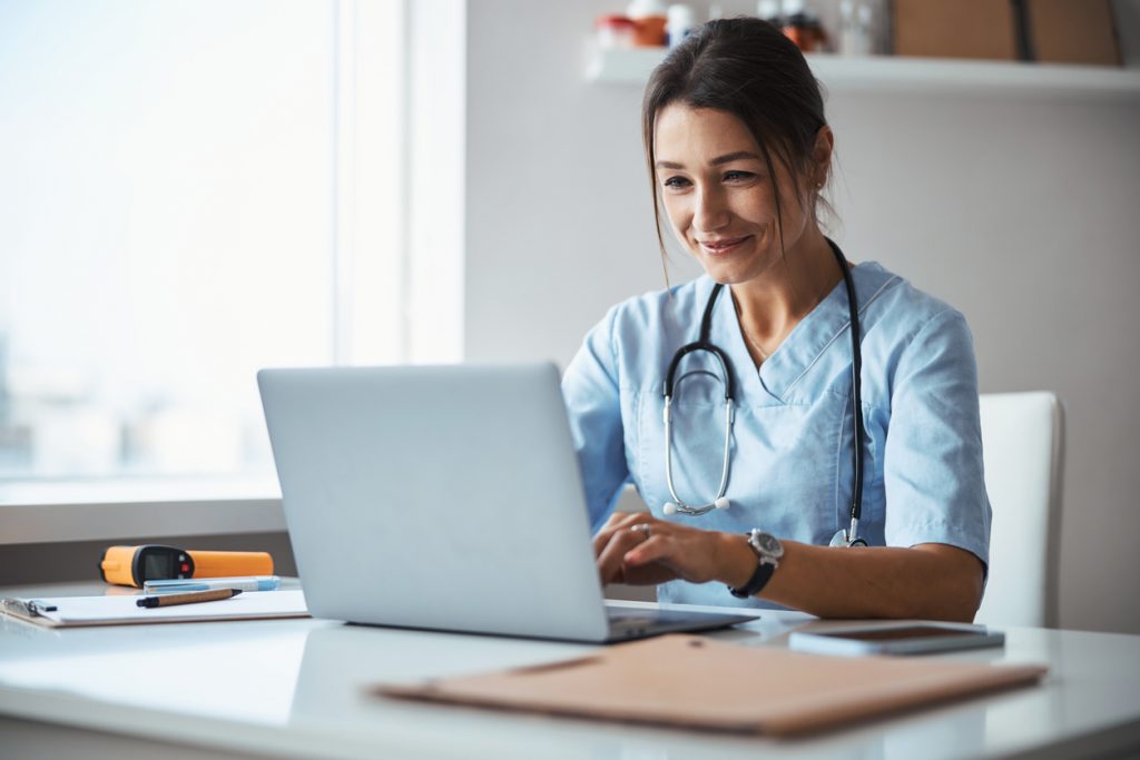 Joyful female doctor using laptop